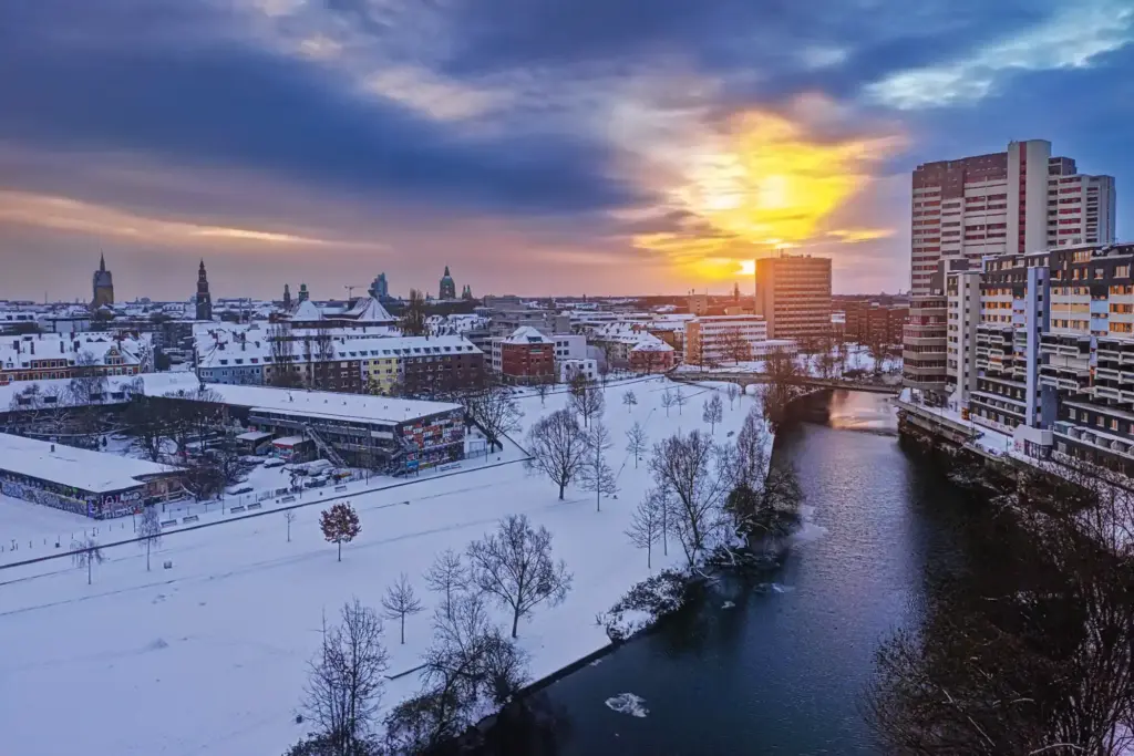 Blick über die verschneite Ihme in Hannover auf das Ihme-Zentrum bei einem dramatischen goldenen Sonnenaufgang im Januar 2026.